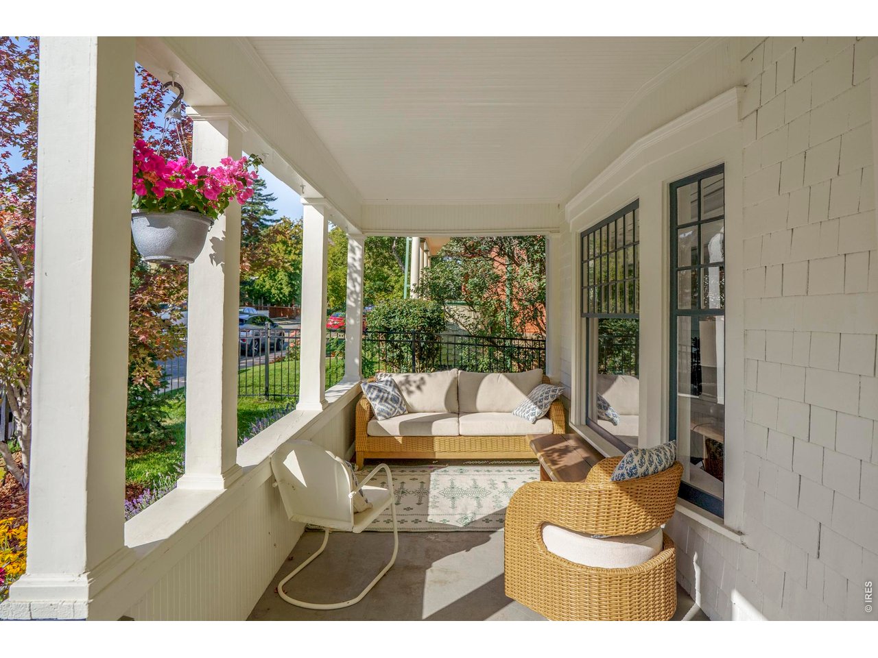 Covered front porch with wicker seating, white columns, and a hanging basket of pink flowers.