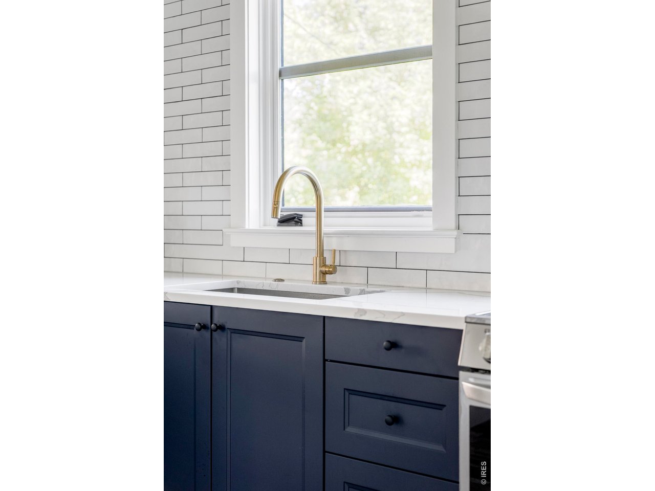 Kitchen with navy cabinets, white subway tile, and a brass faucet beneath a window.