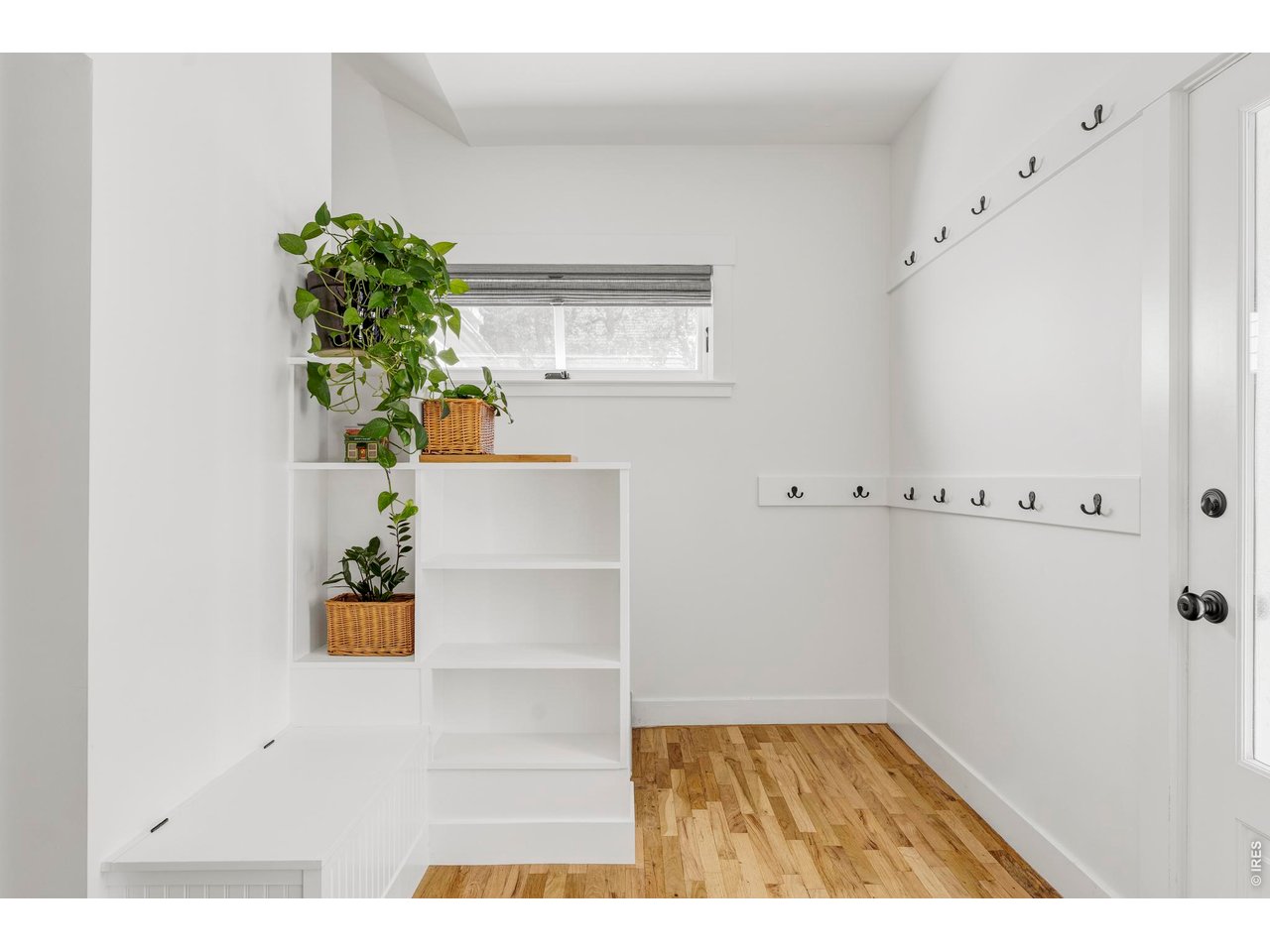 Bright entryway with hardwood floors, wall hooks, built-in shelving, and potted plants.