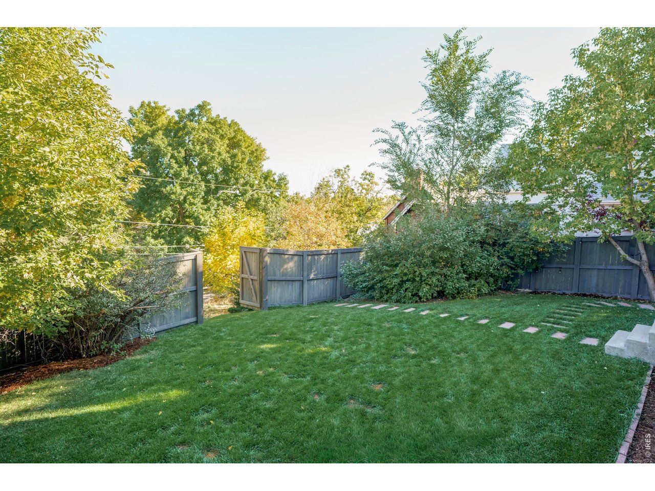 Fenced backyard with a green lawn, mature trees, and a stepping-stone path.