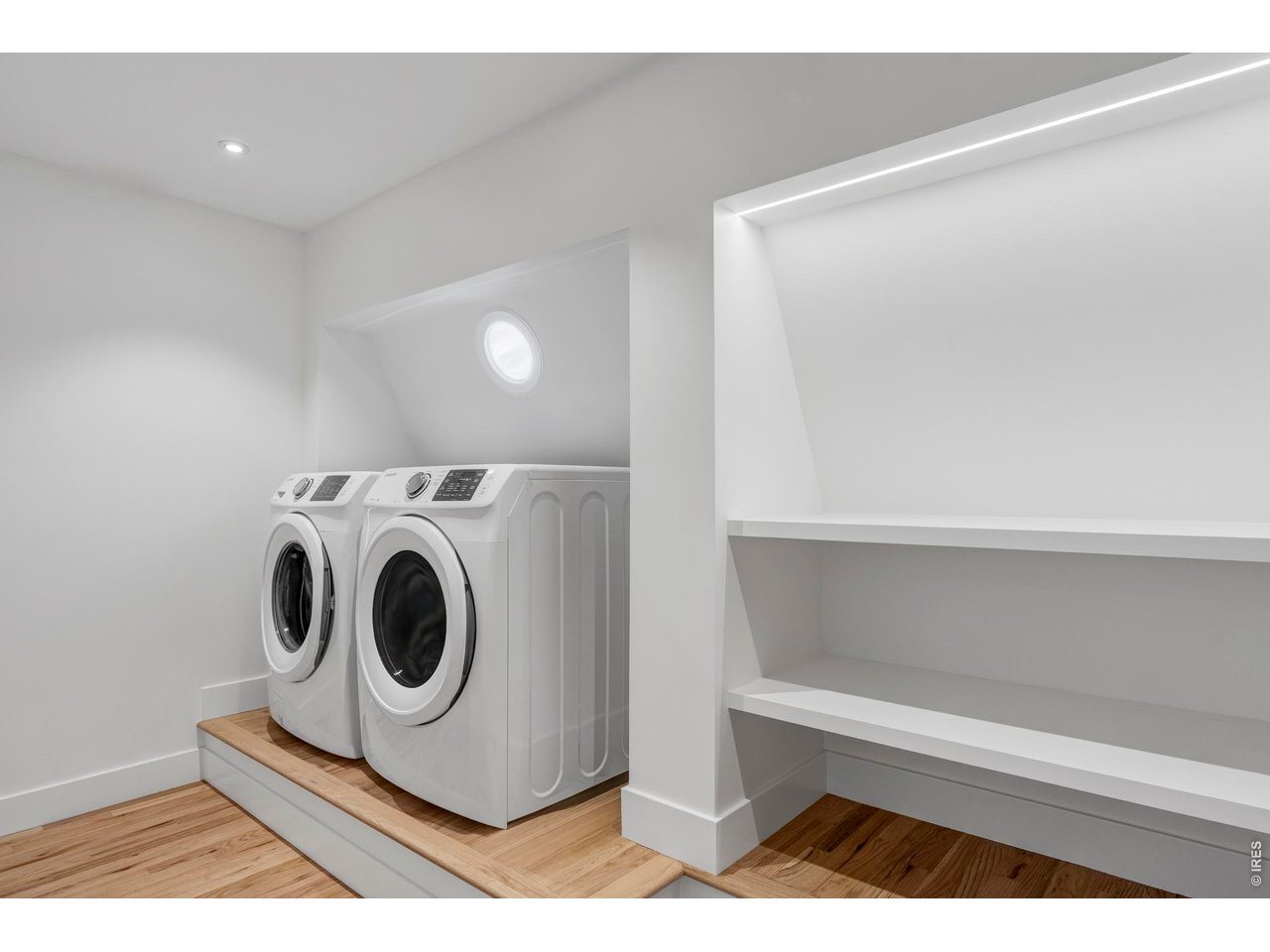 Laundry room with front-loading washer and dryer, built-in shelving, and hardwood floors.
