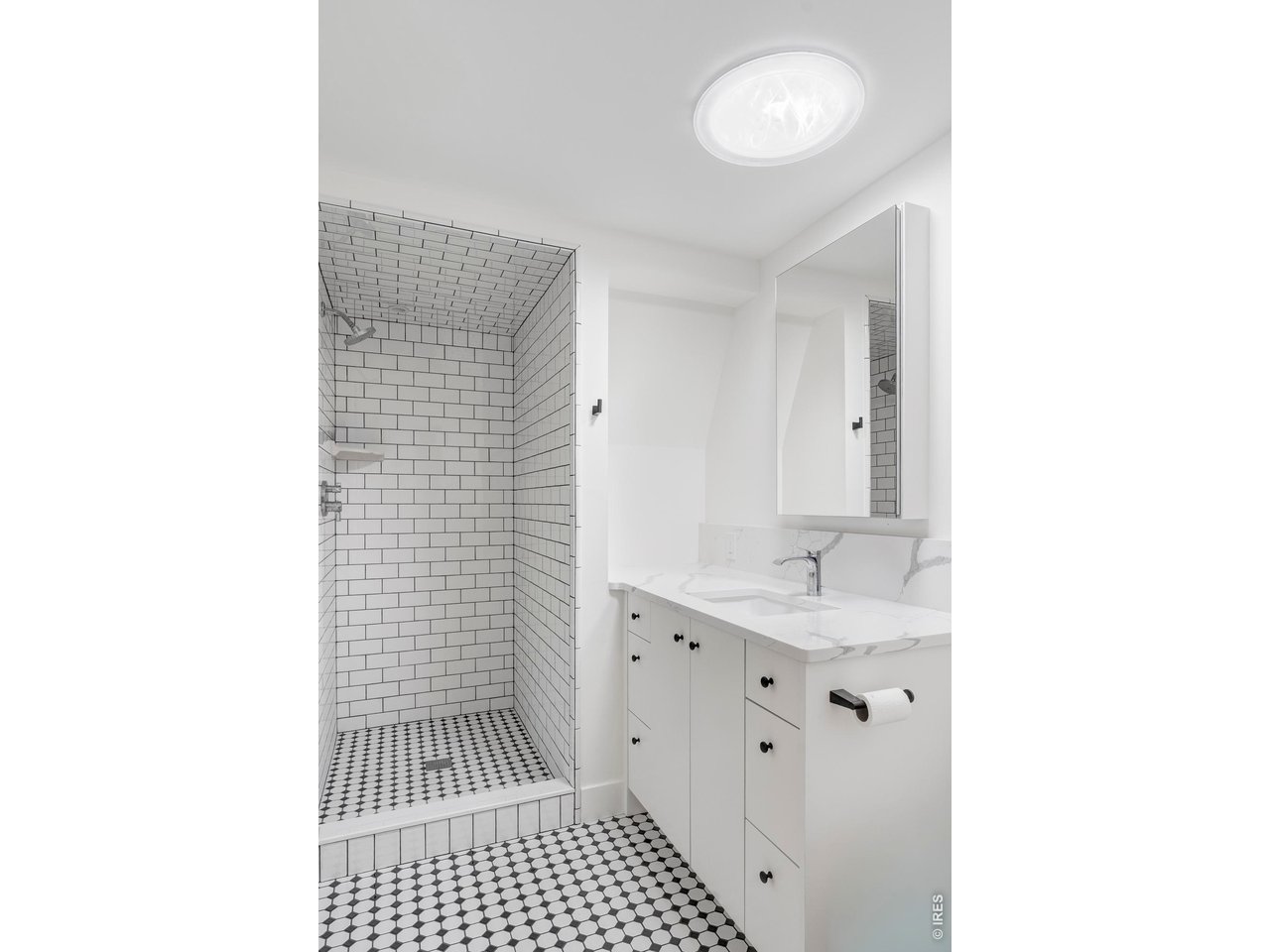 Bright bathroom with tiled shower, black-and-white hexagonal floor, and white vanity.