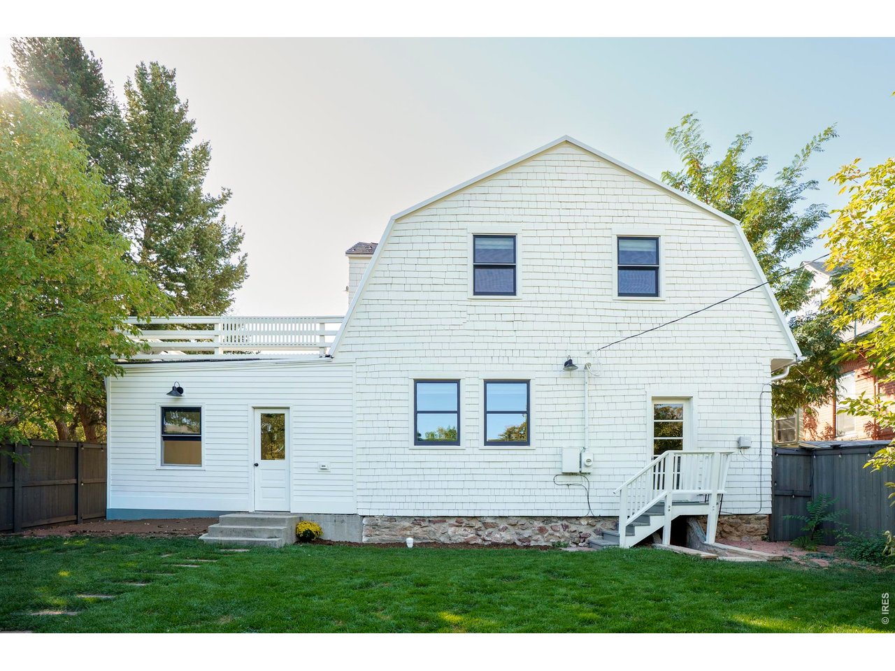 Rear of a white shingle-sided house with a raised deck, lawn, and exterior steps.
