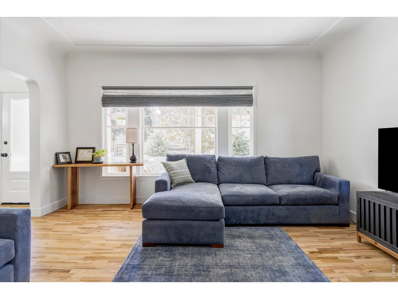 Living room with a blue sectional sofa, hardwood floors, and a large window.