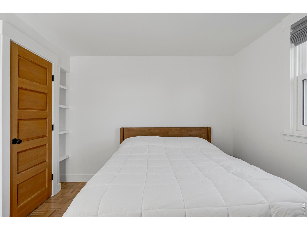 Bedroom with a white-quilted bed, wooden headboard, and built-in wall shelves.