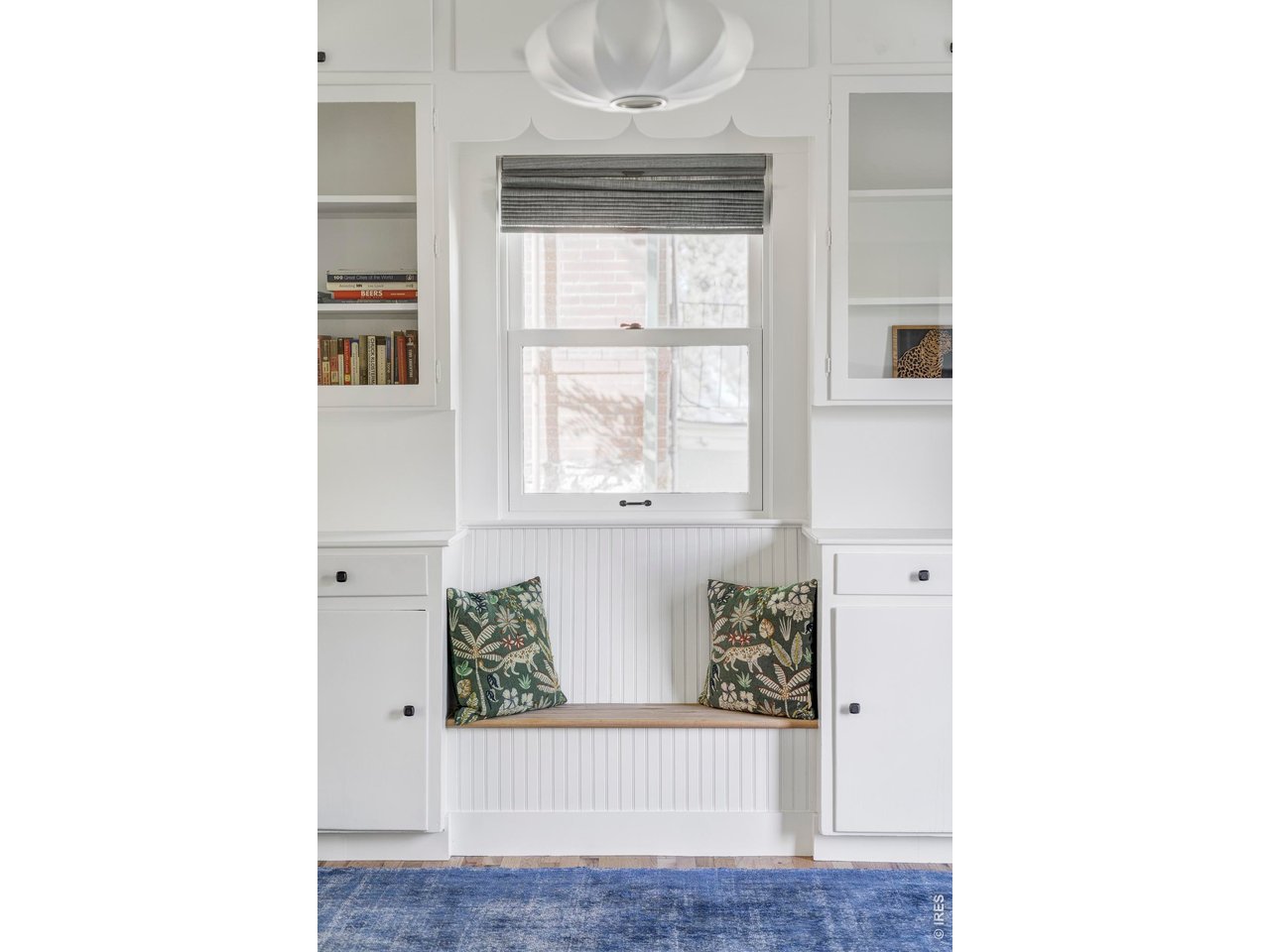Built-in window-seat nook with patterned pillows, white cabinetry, and a blue rug.