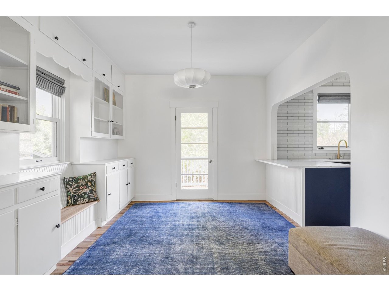 Bright dining area with built-in white cabinetry, a blue rug, and an arched opening to the kitchen.