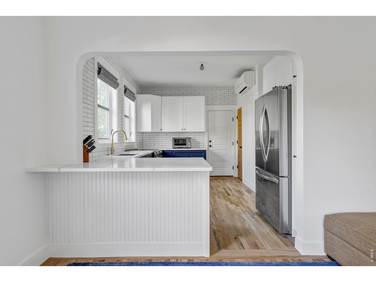 Bright white kitchen with a peninsula, subway tile, stainless steel refrigerator, and hardwood floors.
