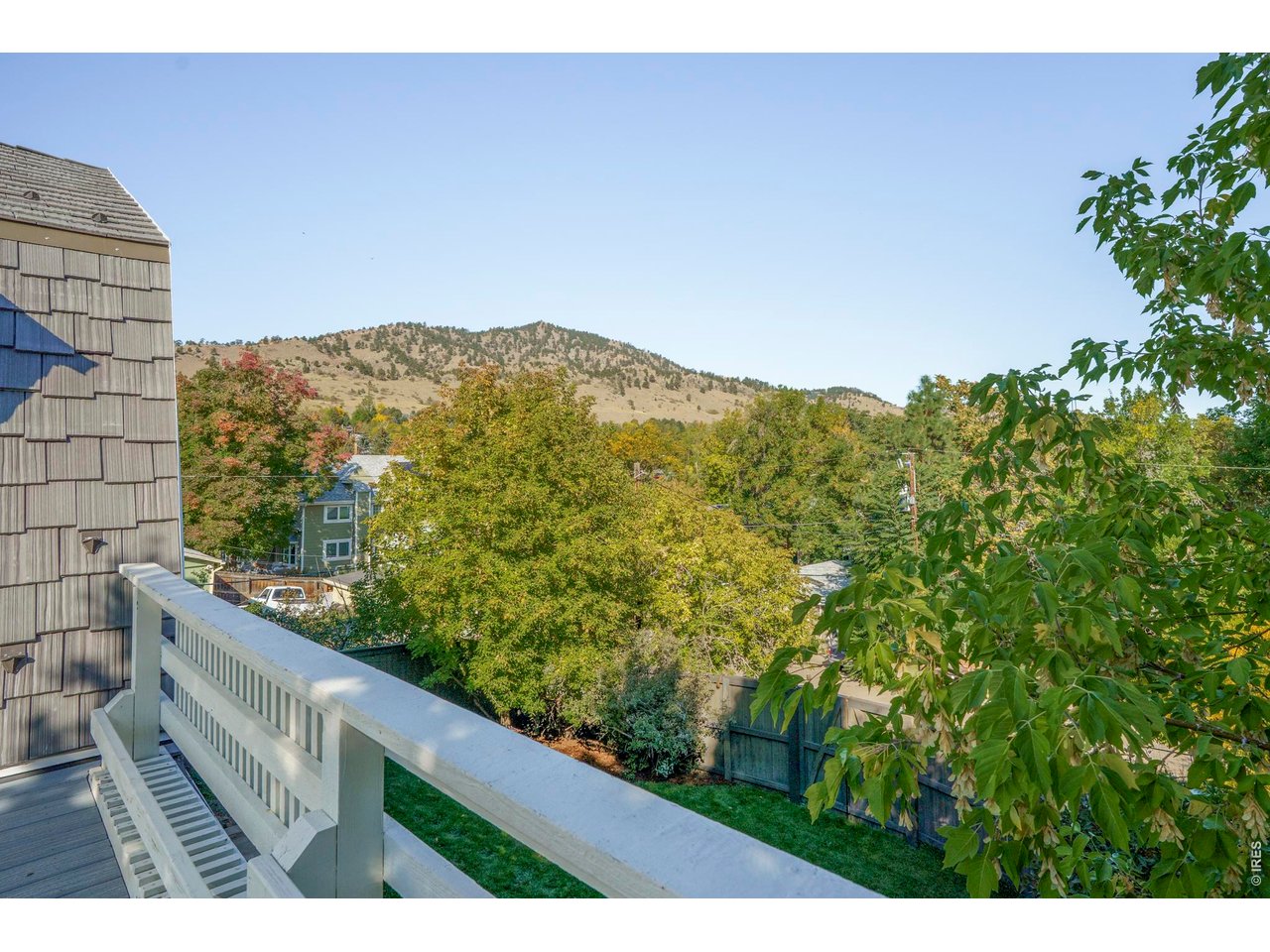 Balcony overlooking autumn trees and foothills, with a white railing and neighboring homes.