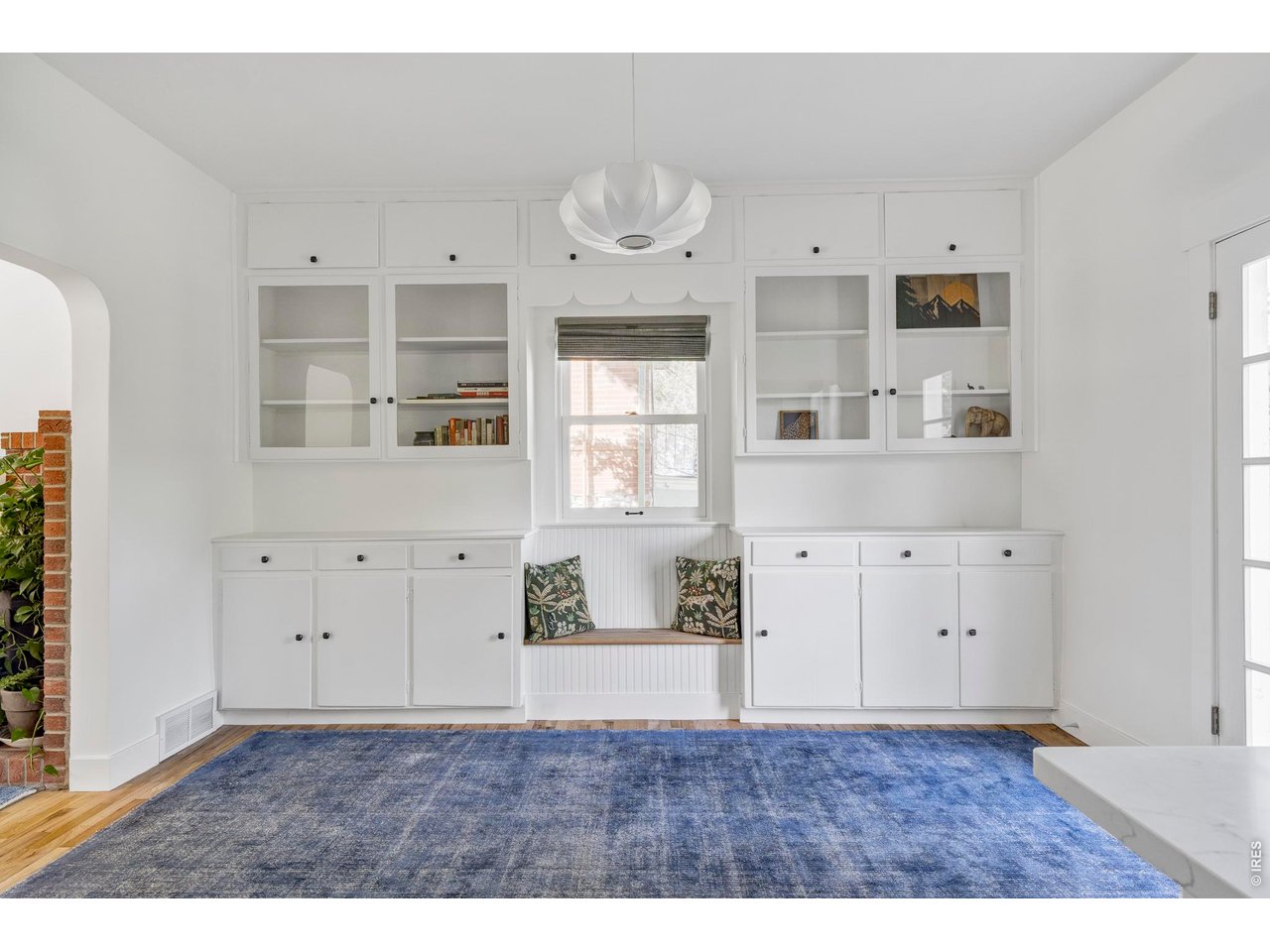 Bright room with white built-ins, a window seat, and a large blue rug.