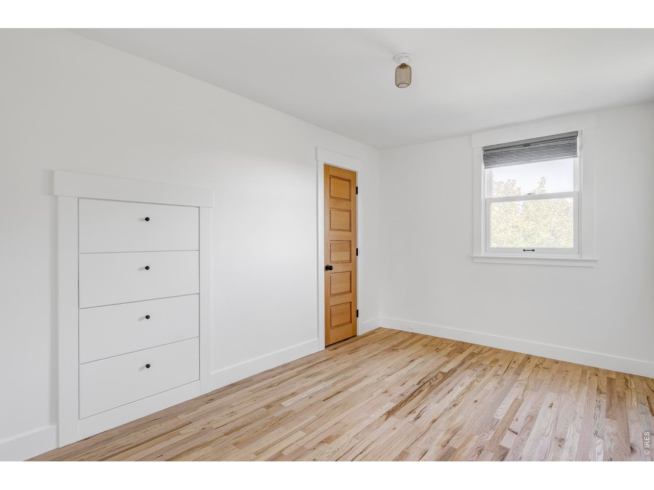 Bright vacant bedroom with a built-in white dresser, wood door, and hardwood floors.
