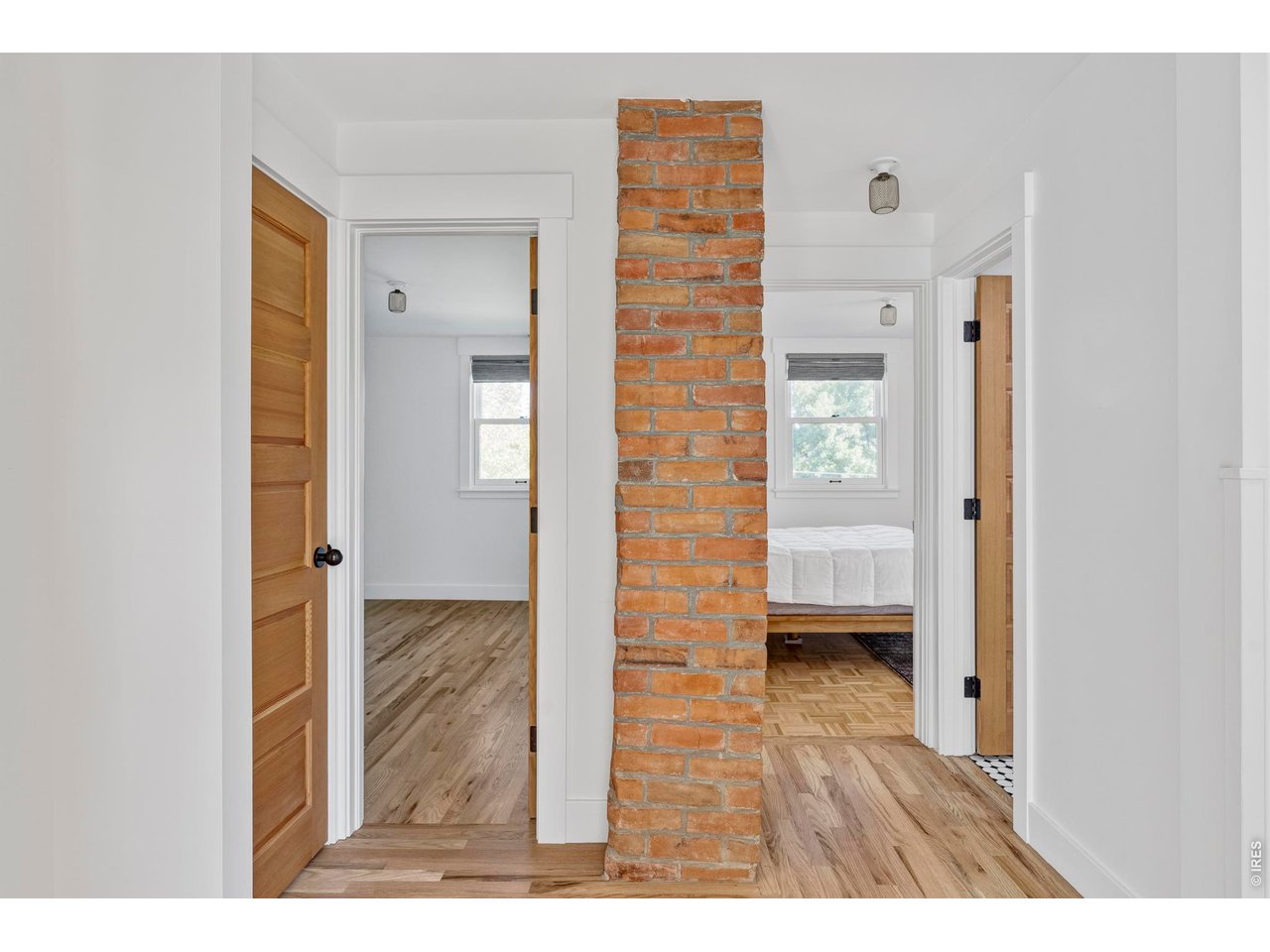 Hallway with an exposed brick column, wood floors, and open doorways to two rooms.