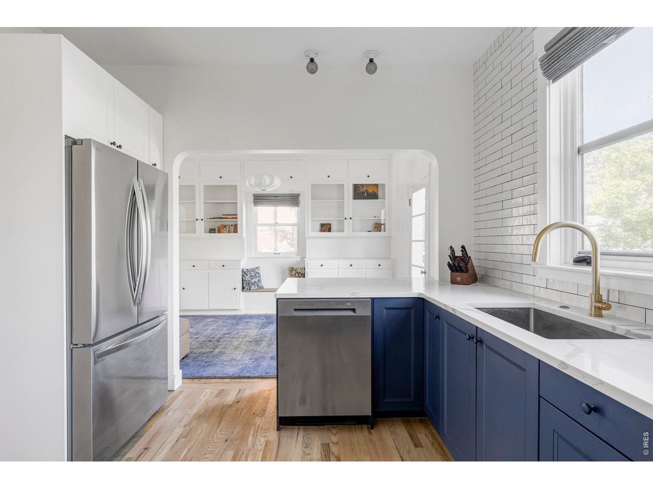 Bright white kitchen with navy cabinets, stainless steel appliances, and a large farmhouse sink.
