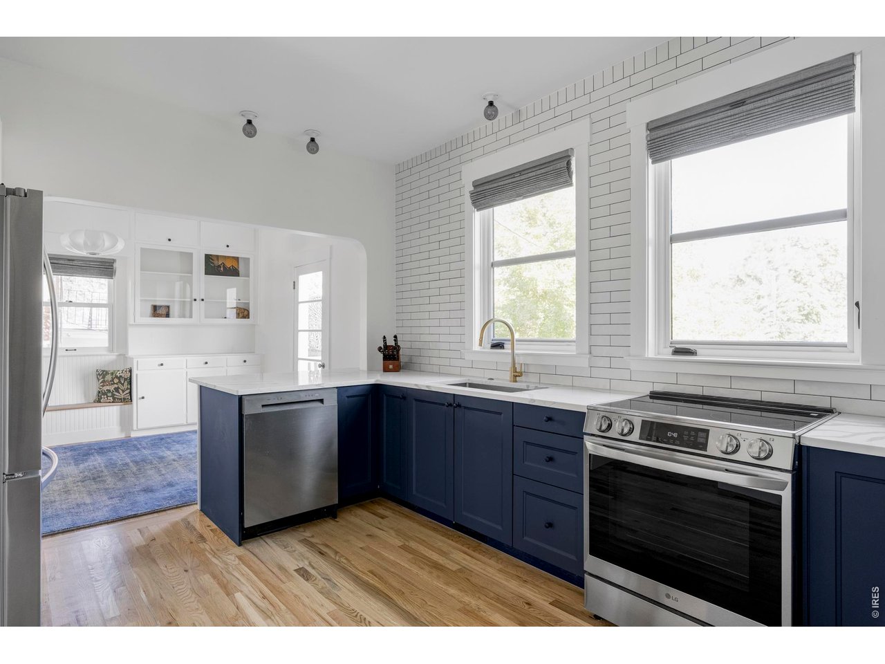 Kitchen with navy cabinets, white tile walls, stainless steel appliances, and hardwood floors.