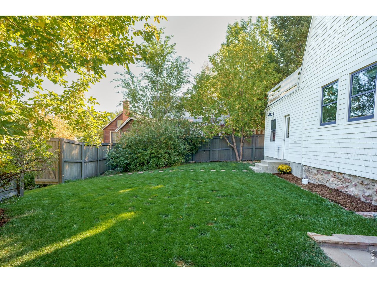 Fenced backyard with a broad lawn, mature trees, and a white-sided home.