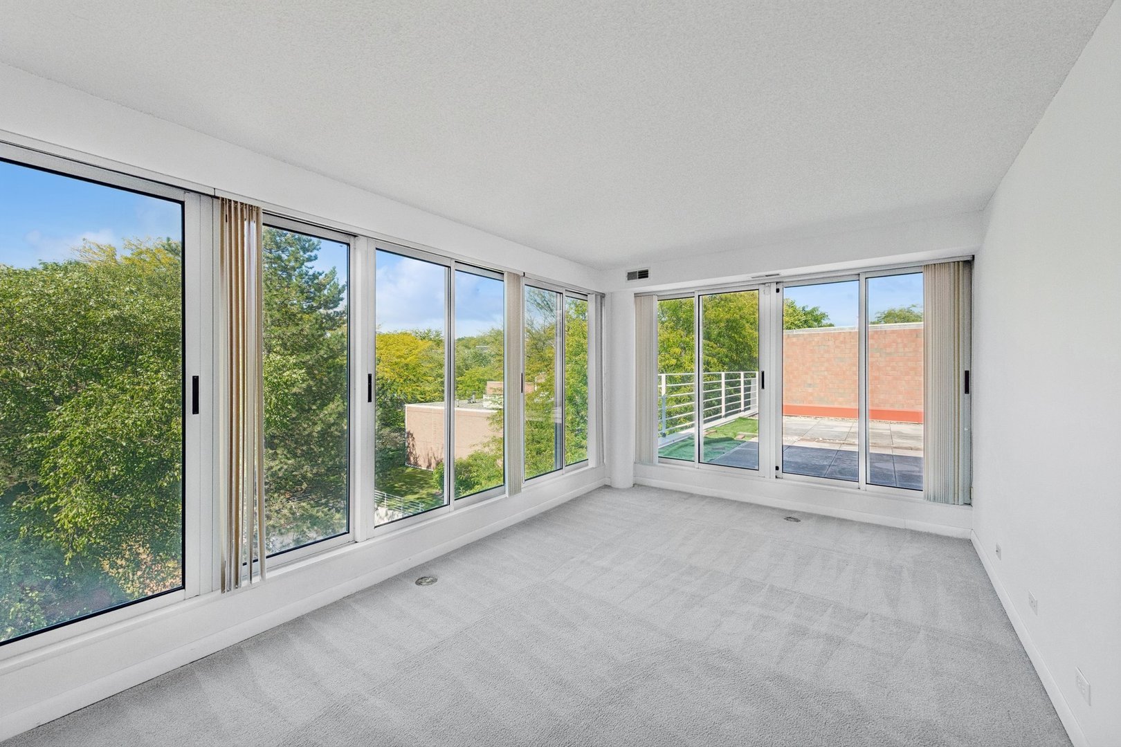 Empty carpeted room with floor-to-ceiling windows and sliding doors to a balcony.