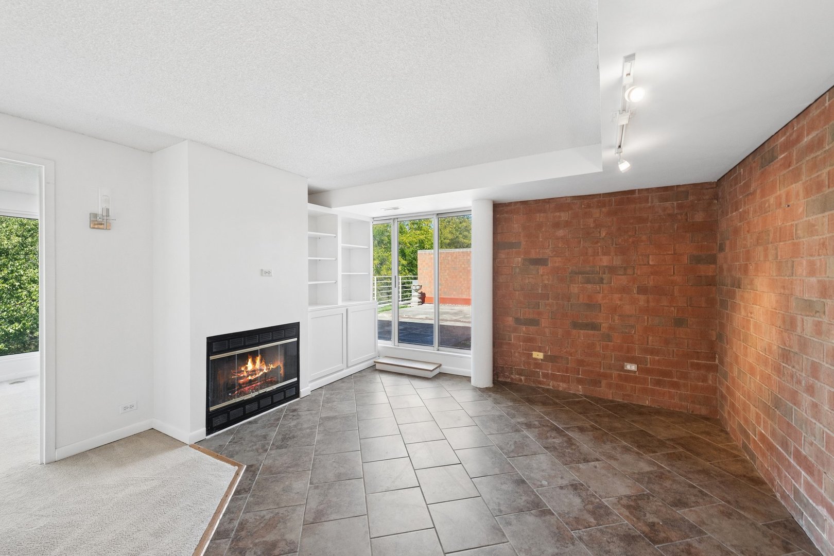 Unfurnished living area with a brick accent wall, tiled floor, fireplace, and sliding doors to a terrace.
