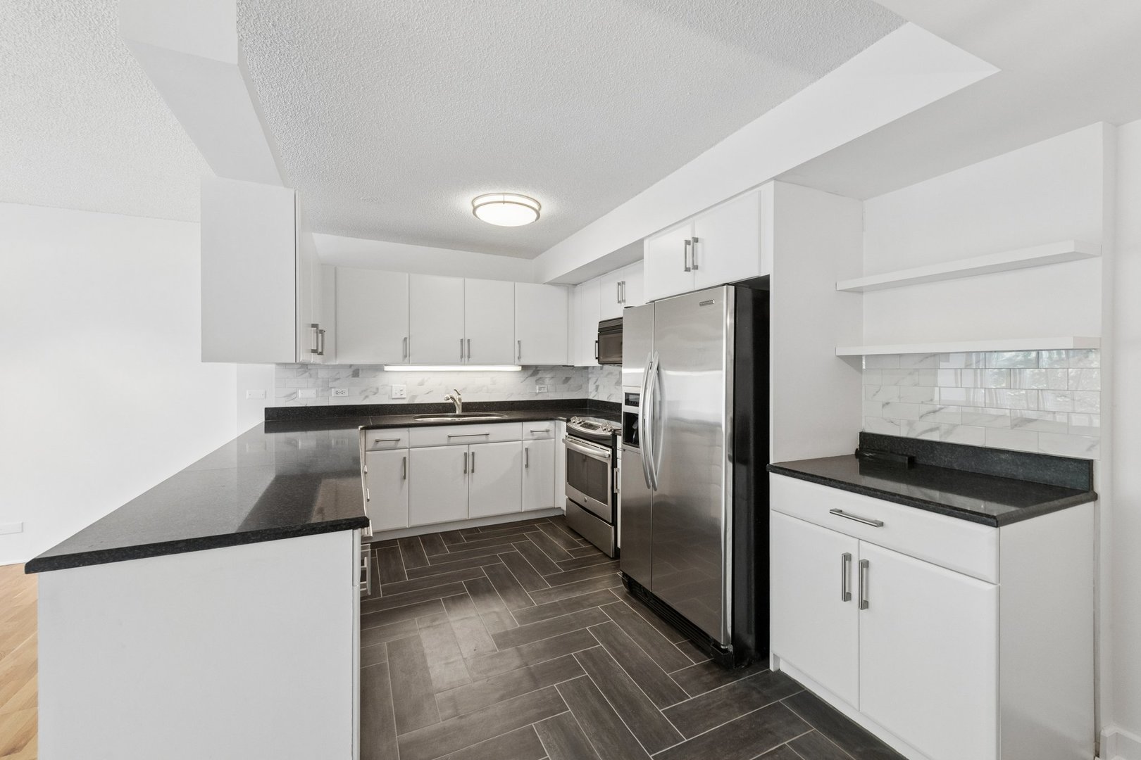 Kitchen with white cabinets, black countertops, stainless steel appliances, and dark gray tile flooring.