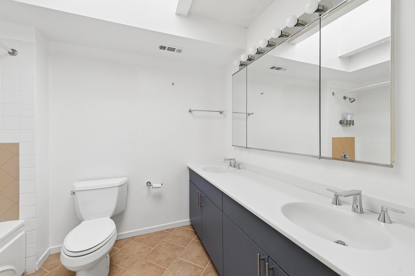 Bathroom with a double-sink vanity, large mirror, toilet, and tiled tub and shower.
