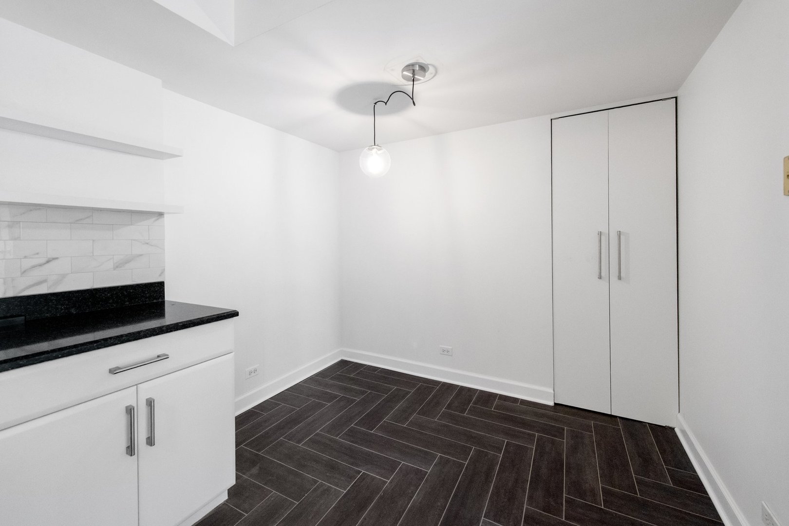Empty kitchen and dining area with black countertops, white cabinetry, dark herringbone tile flooring, and a double-door closet.