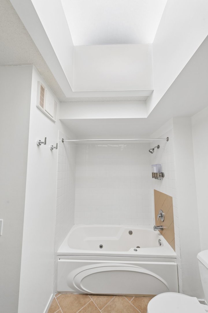 Bathroom with a built-in jetted tub, white tiled shower alcove, and high recessed ceiling.