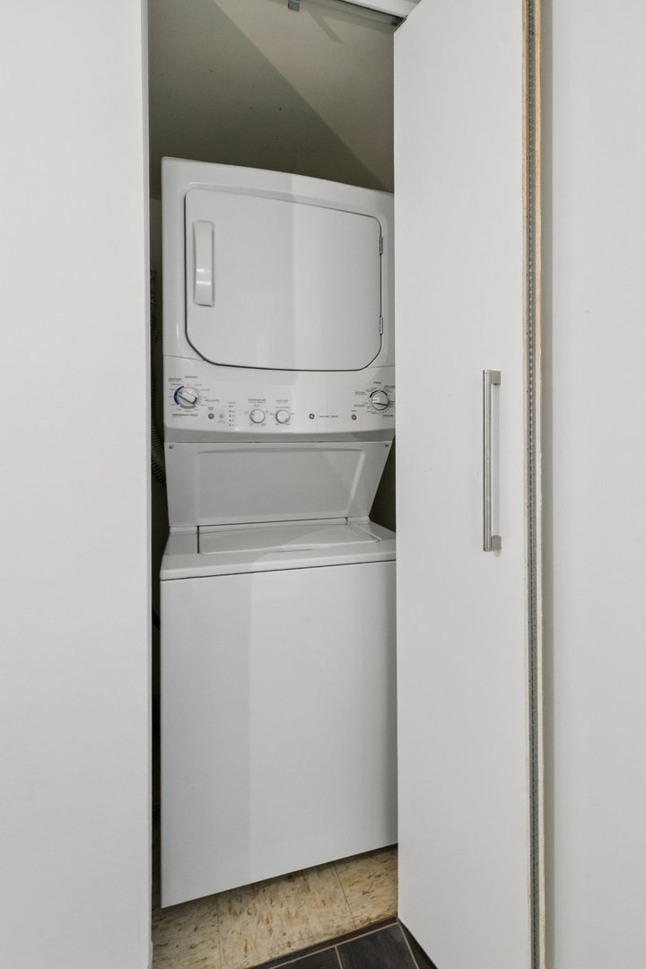 Stacked washer and dryer in a narrow laundry closet with the door open.