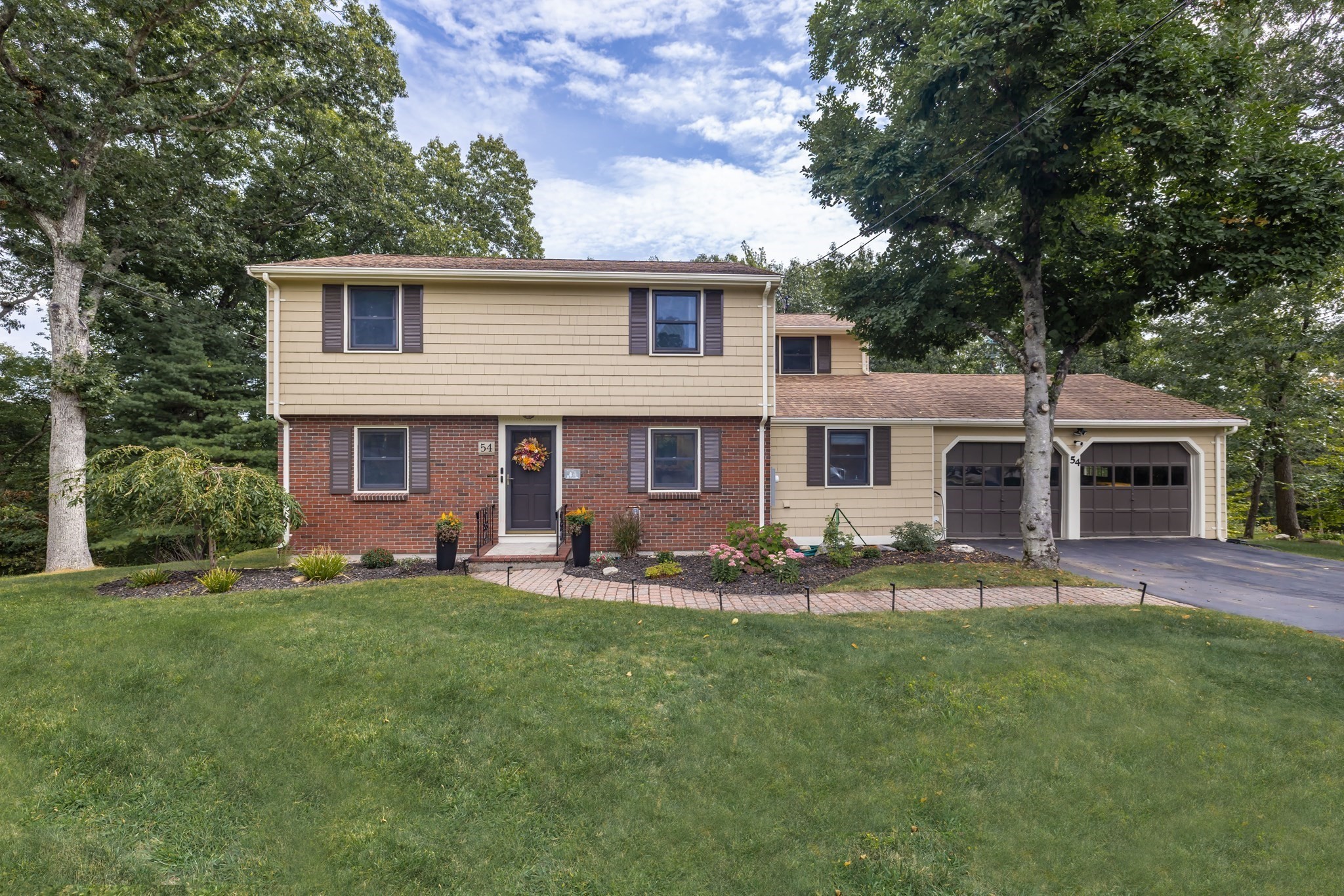 Two-story beige-and-brick home with an attached two-car garage, landscaped garden, and broad lawn.