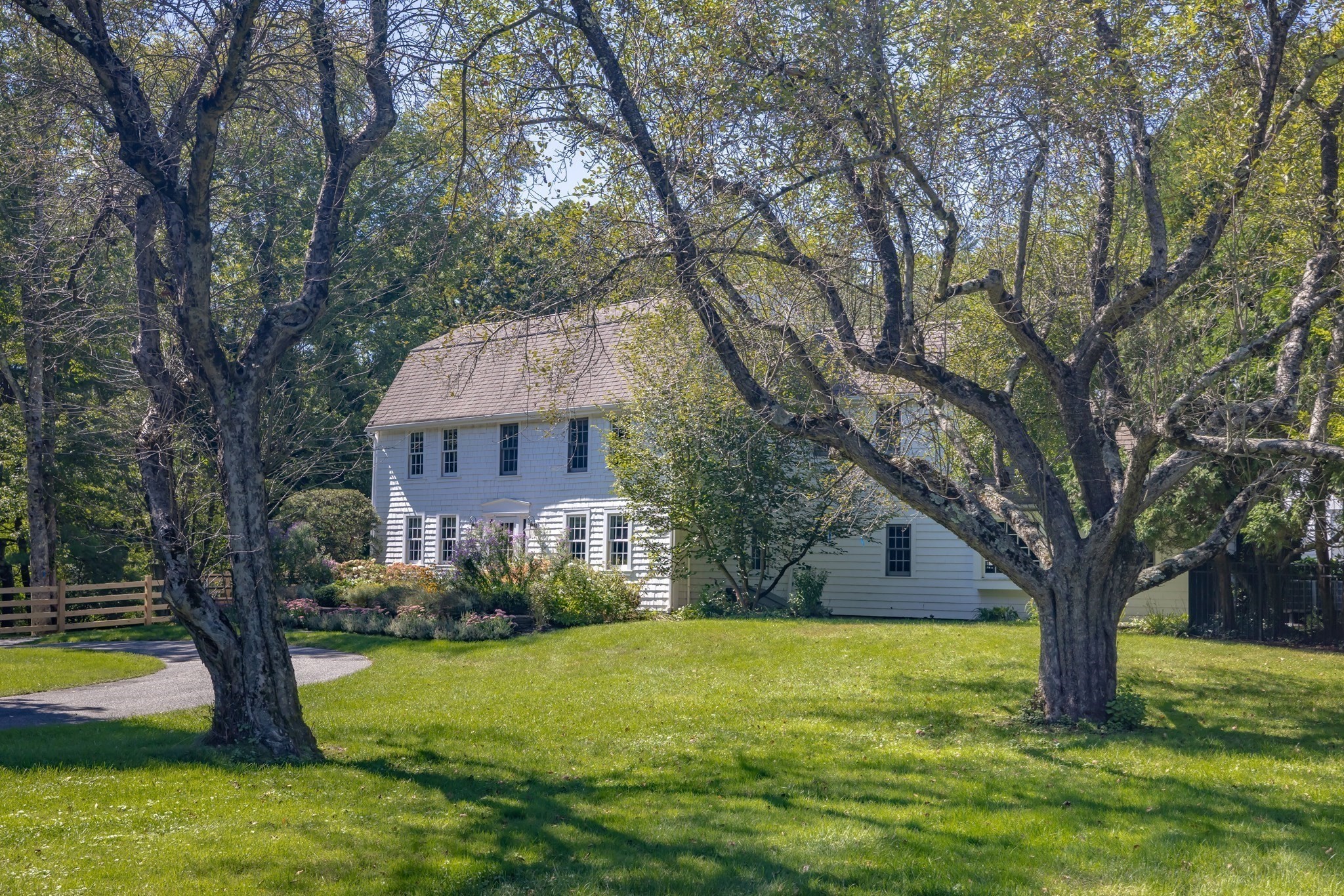 White two-story house framed by mature trees, with a landscaped garden and curved driveway.
