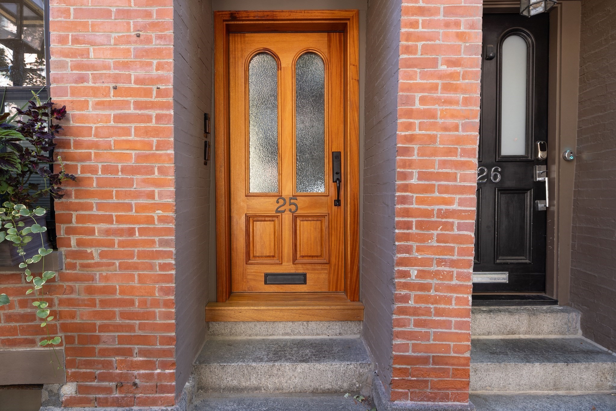 Brick townhouse entrance with a wood-and-glass door numbered 25 beside a black door numbered 26.