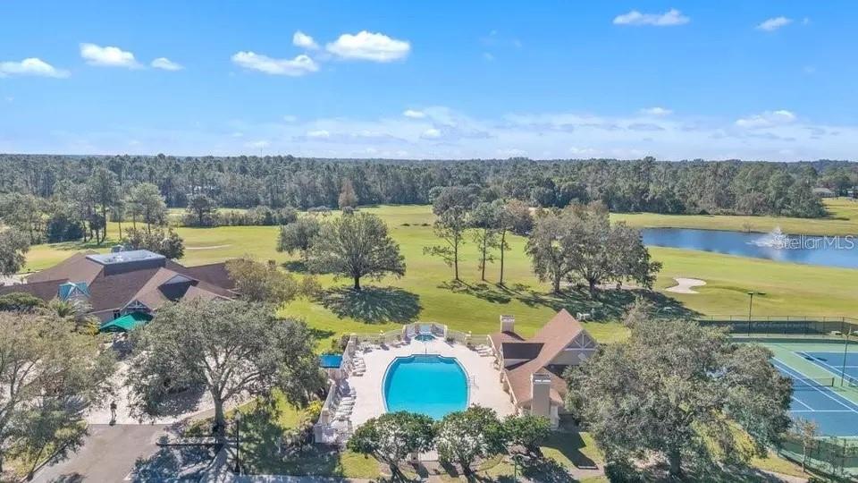 Aerial view of a community pool, tennis courts, lake, and golf course.