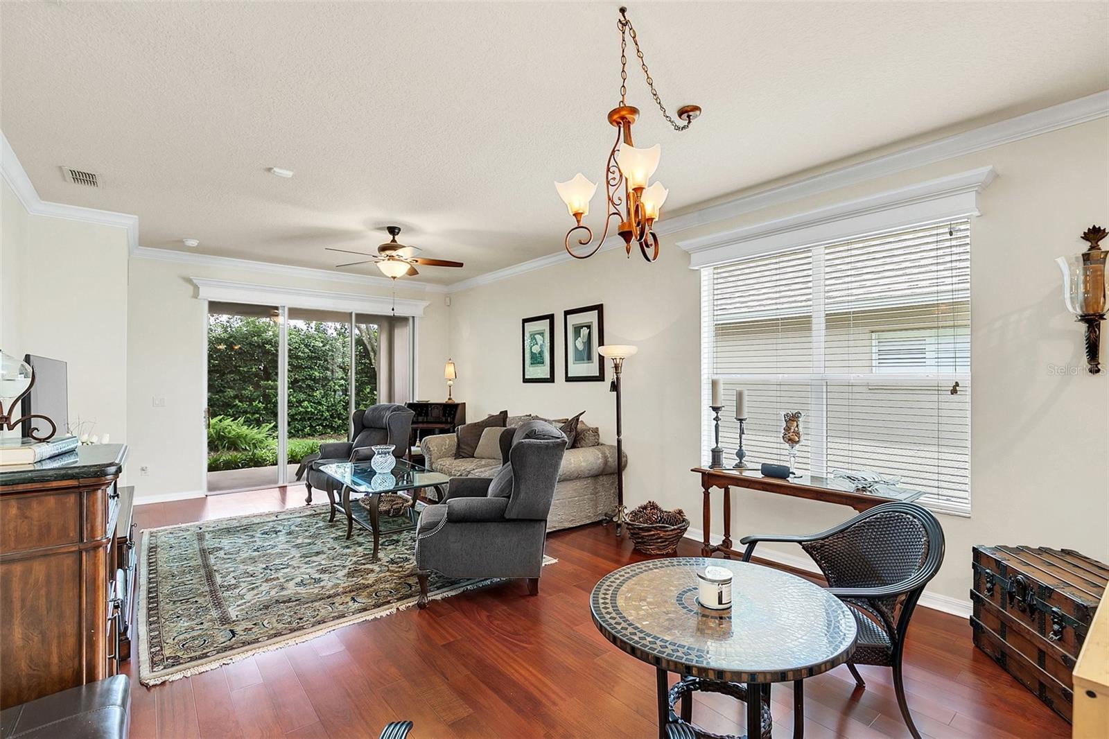 Furnished living room with hardwood floors, large windows, and sliding glass doors overlooking greenery.