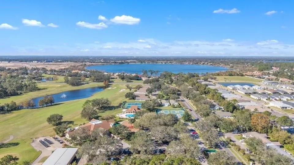 Aerial view of homes beside a golf course, ponds, tennis courts, and a lake.