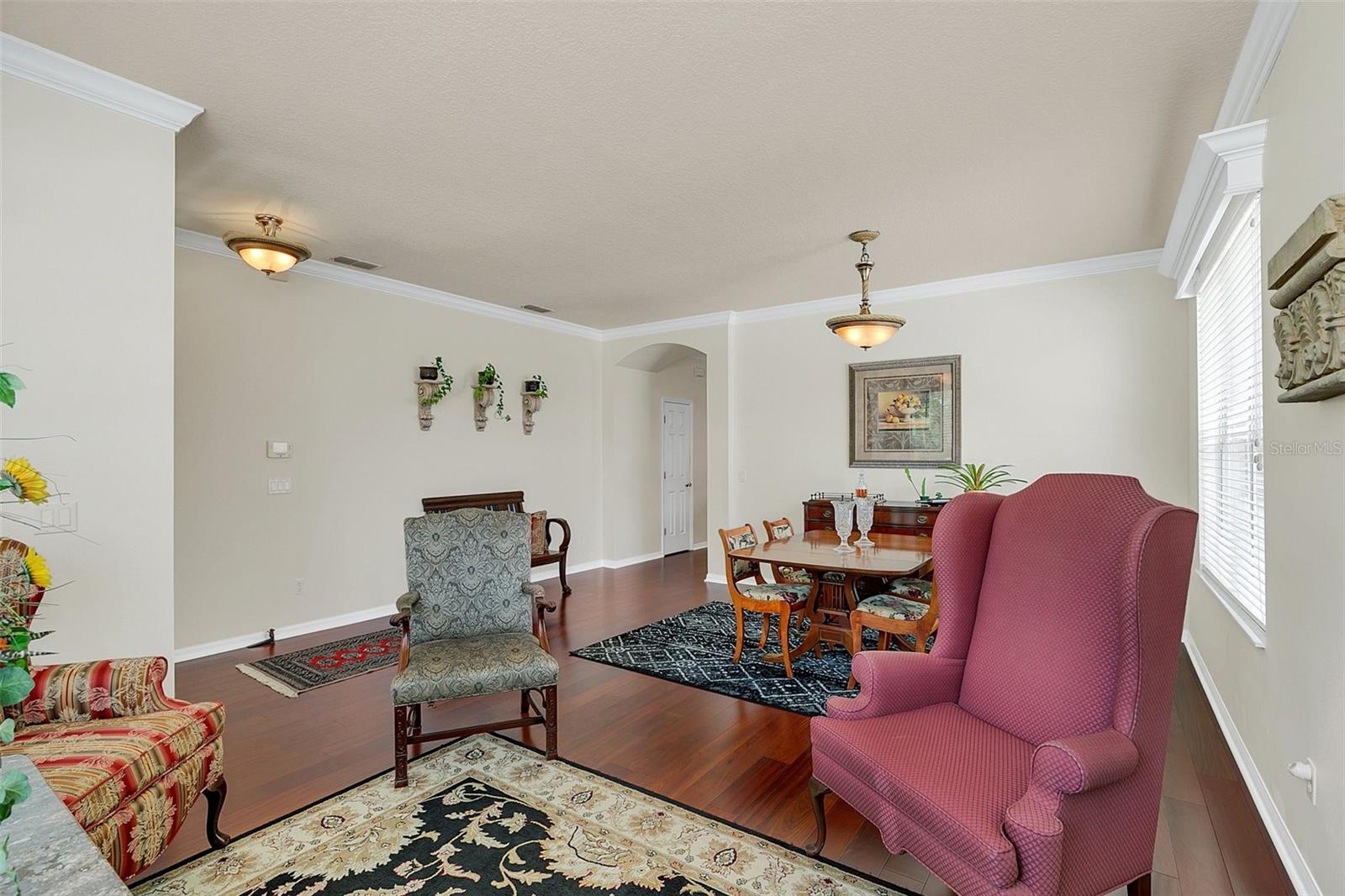 Furnished living and dining area with dark wood floors, patterned rugs, and colorful upholstered armchairs.