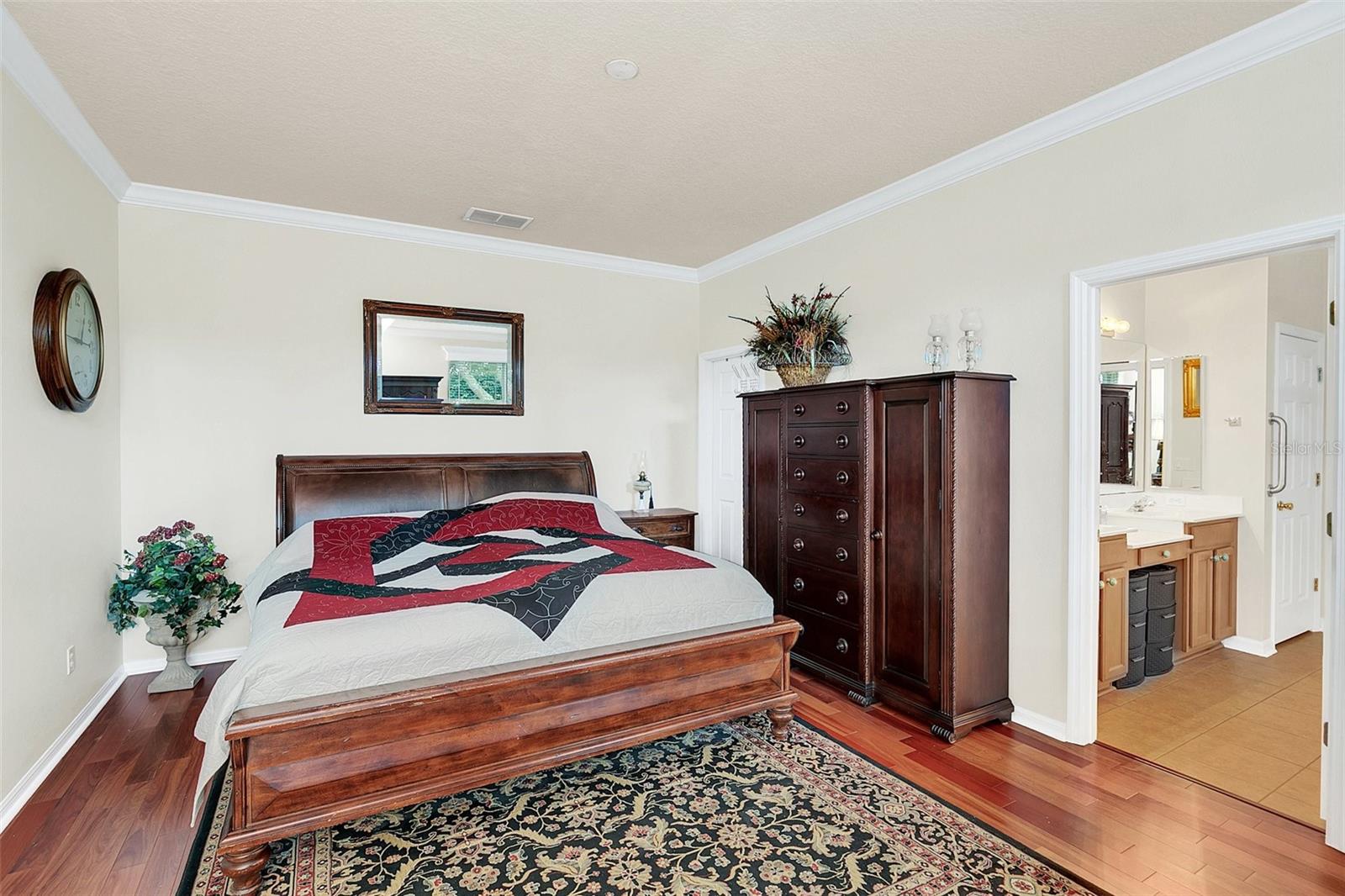 Furnished bedroom with dark wood furniture, a patterned rug, and an adjoining bathroom vanity.