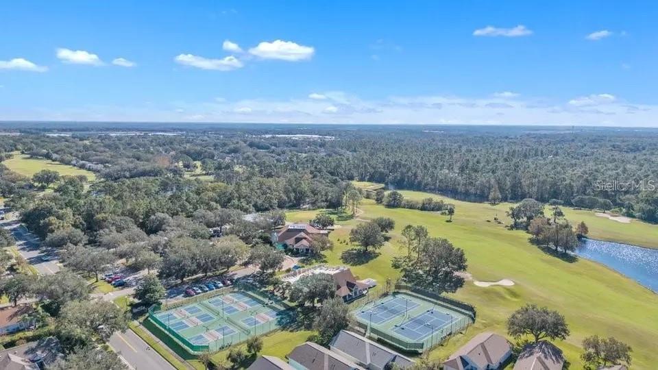 Aerial view of a golf course community with tennis courts, sand bunkers, and a pond.