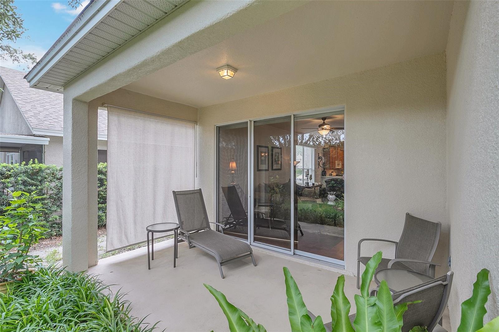 Covered patio with lounge chairs, a retractable shade screen, and sliding glass doors.