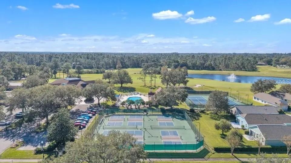 Aerial view of community tennis courts, a swimming pool, and a pond surrounded by trees.