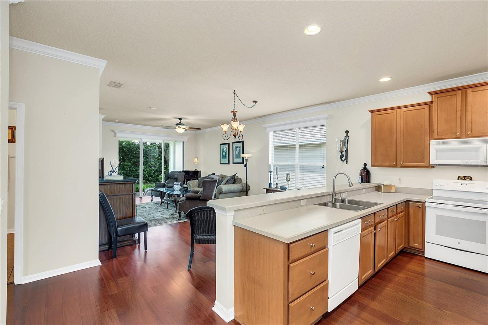 Open kitchen with warm wood cabinets and white counters overlooking a furnished living room.