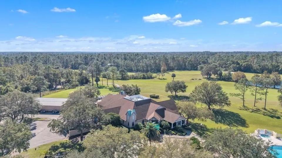 Aerial view of a large home surrounded by lawns and mature trees, with a swimming pool and pond nearby.