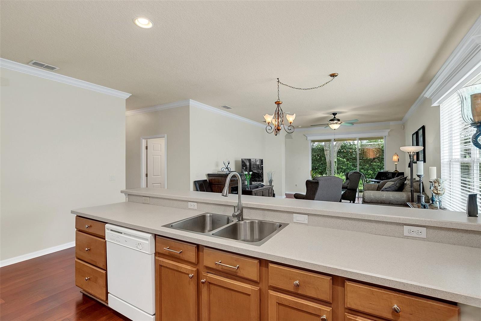 Kitchen with a double-basin sink and wood cabinets opening onto a furnished living room.