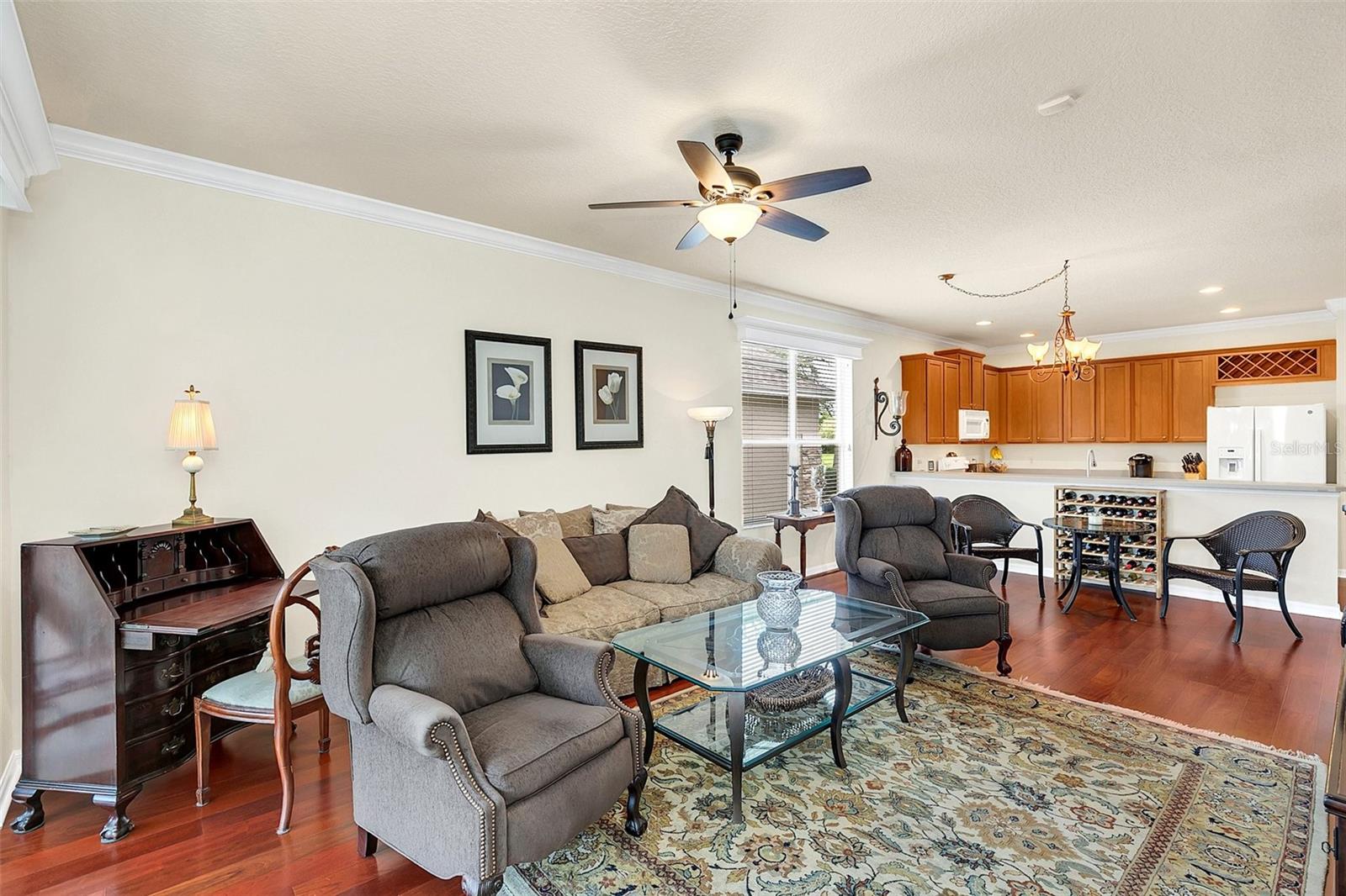 Furnished living room with gray seating, patterned rug, and open kitchen with wood cabinets.