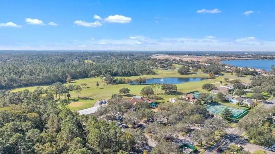Aerial view of homes beside a golf course, ponds, and tennis courts.