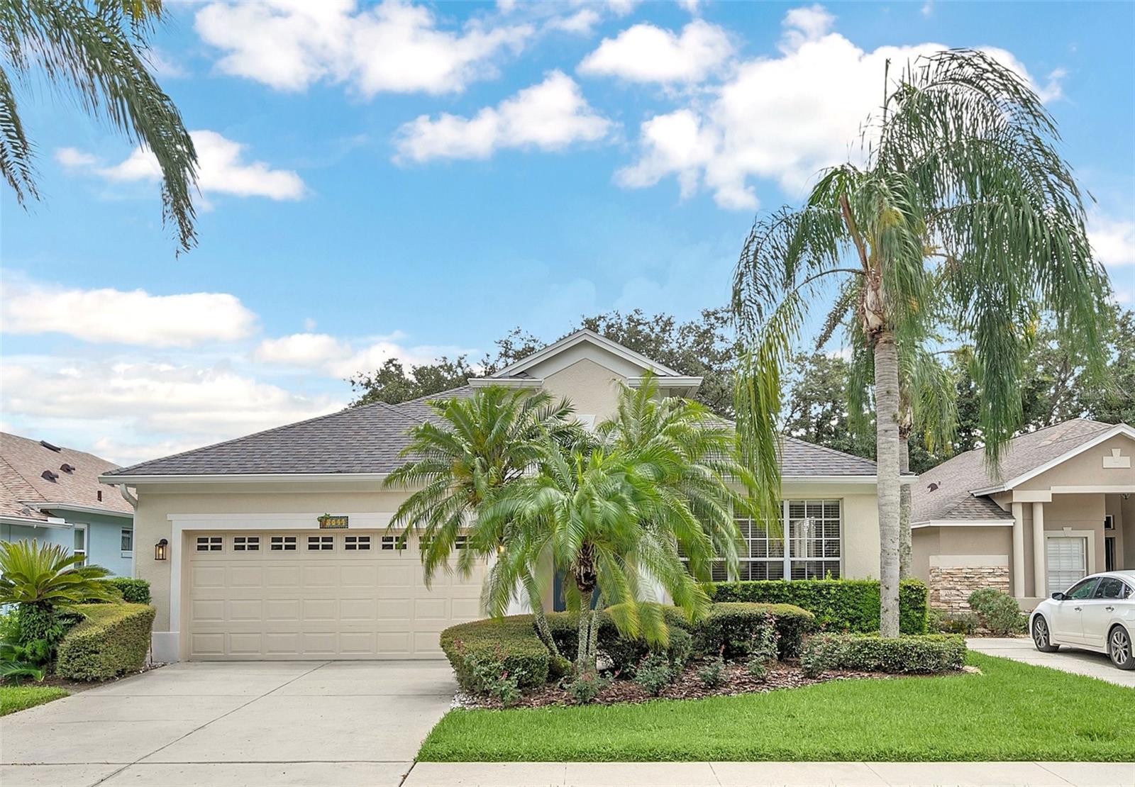 Single-story beige home with a two-car garage, palm trees, and landscaped front yard.