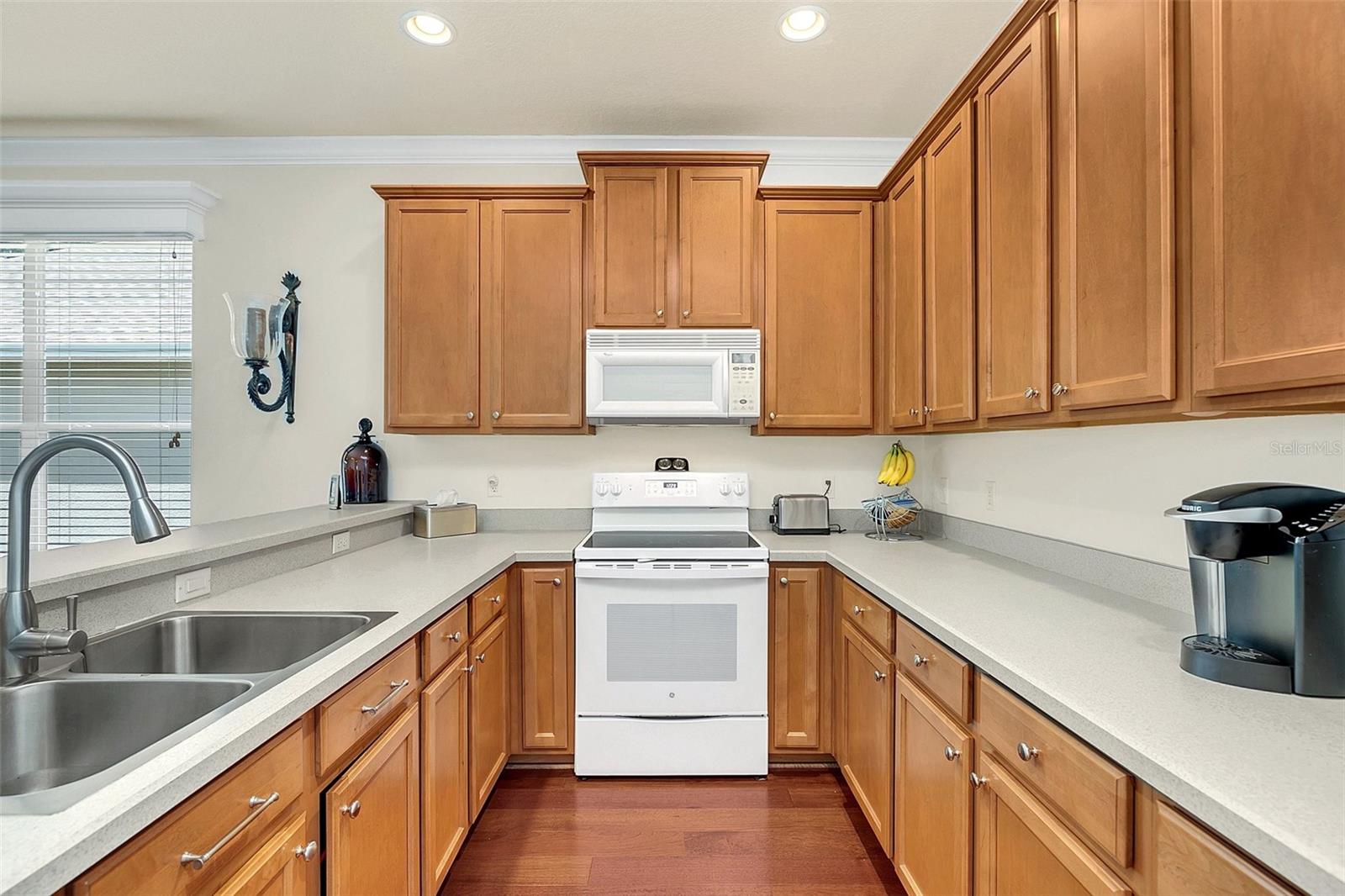 Kitchen with warm wood cabinetry, light countertops, double sink, and white range and microwave.