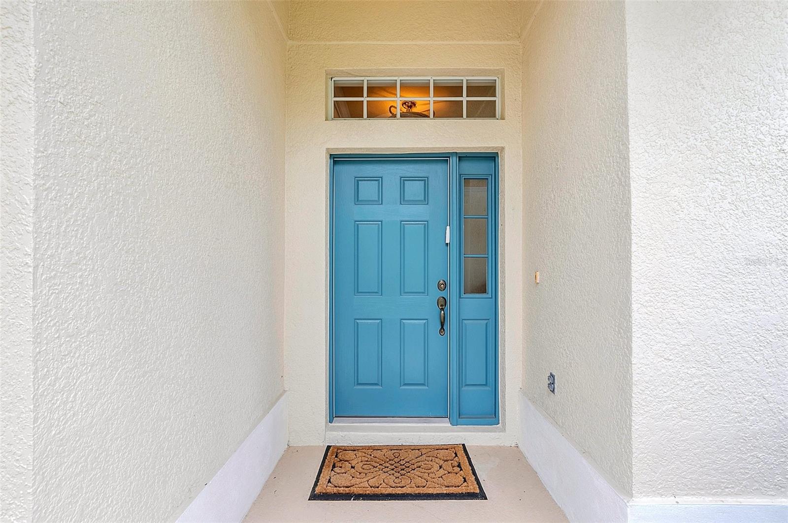 Covered entry with a bright blue front door, glass sidelights, and a patterned doormat.