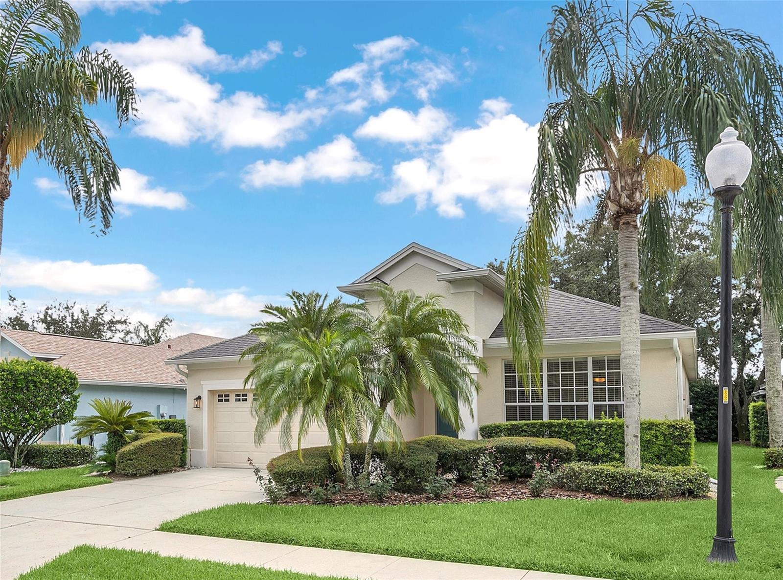 Beige home with an attached garage, trimmed hedges, and palm trees along the front lawn.