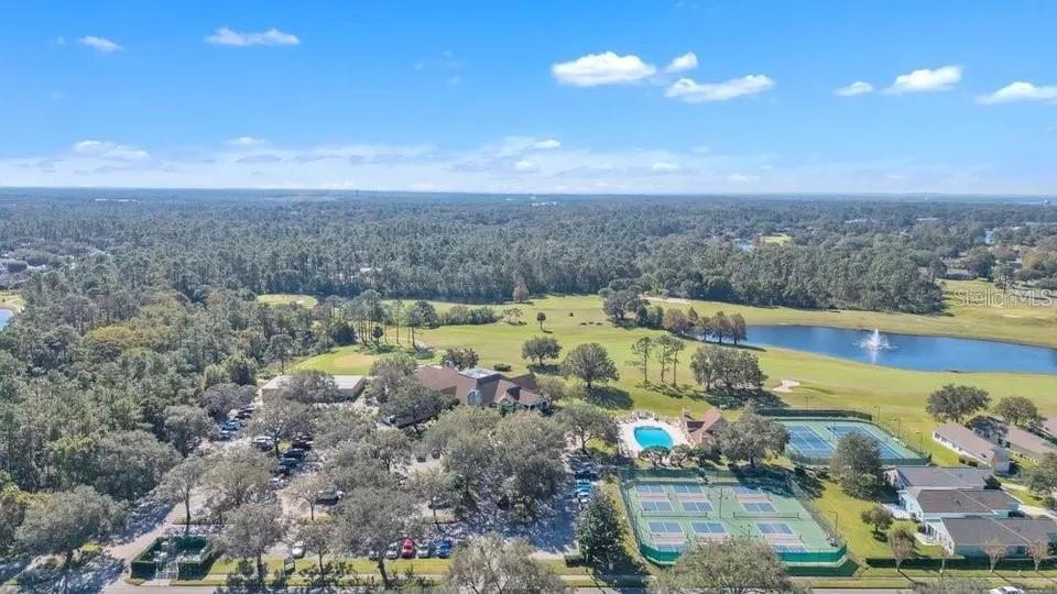 Aerial view of a community with a lake, pool, and tennis courts.