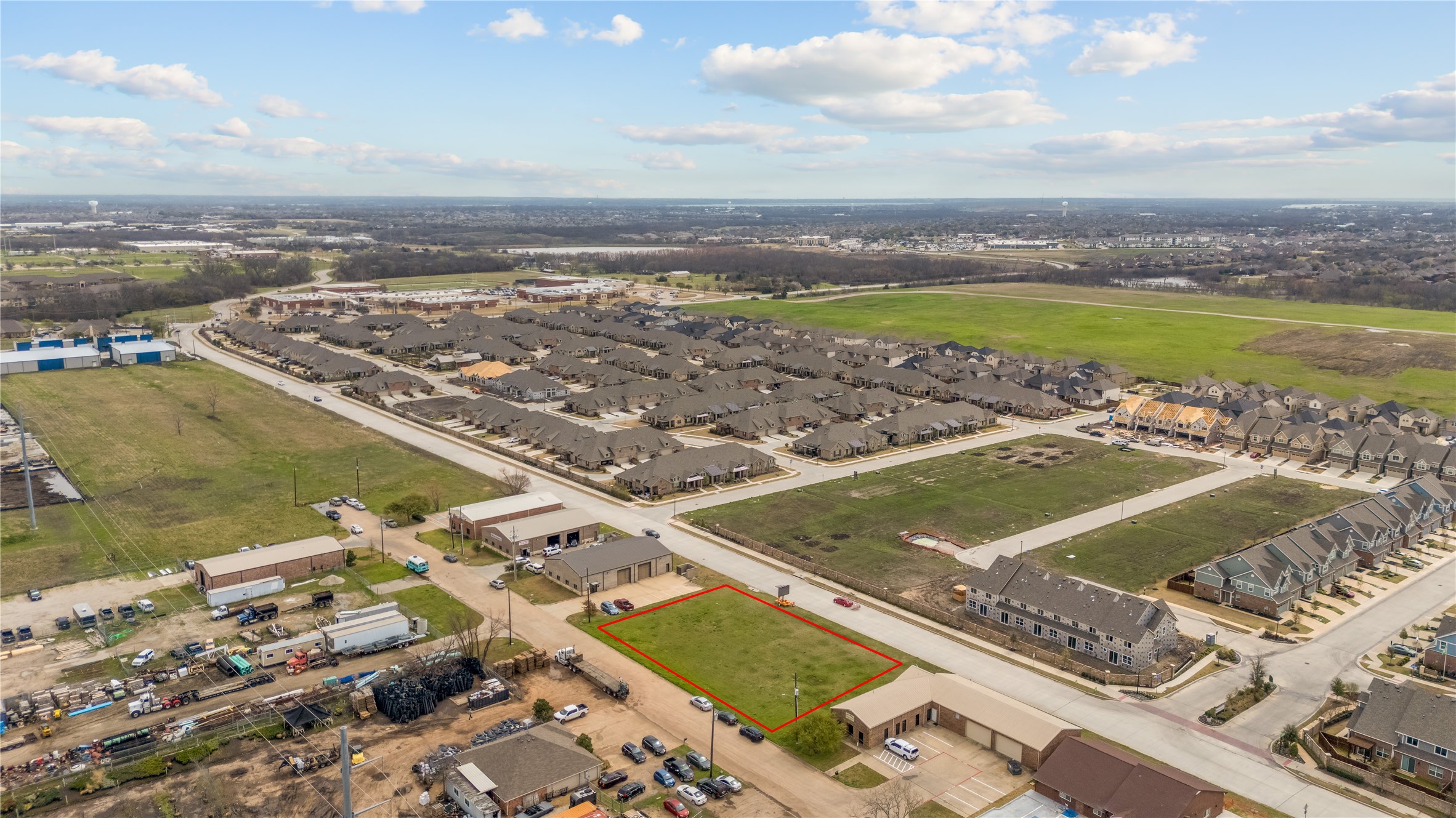 Aerial view of a vacant grassy lot outlined in red amid homes and neighborhood streets.