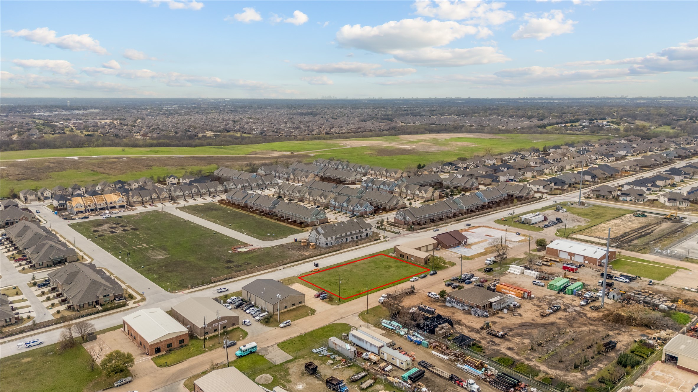 Aerial view of a vacant lot outlined in red amid homes and commercial construction.