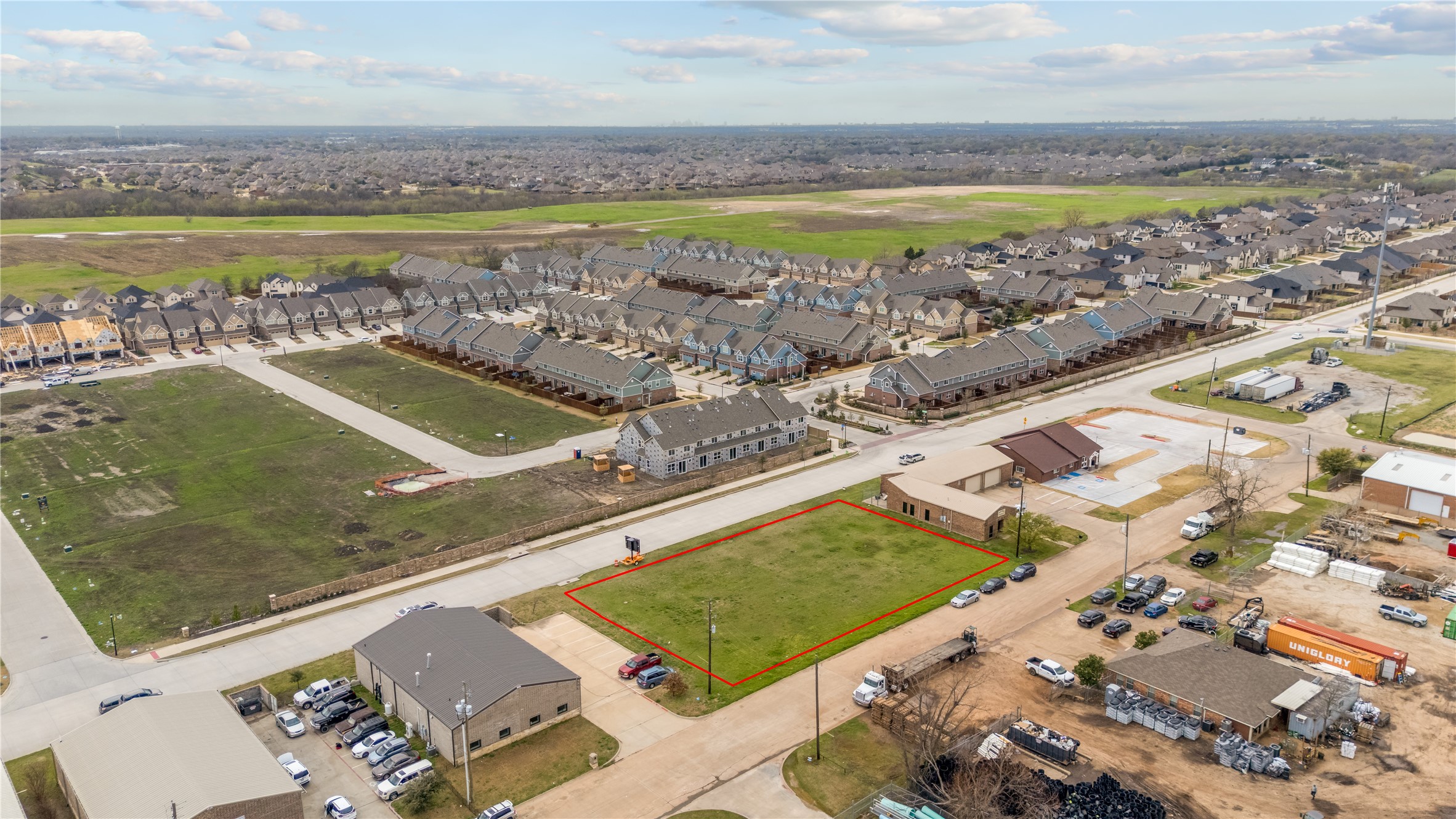 Aerial view of a grassy lot outlined in red among homes and construction sites.
